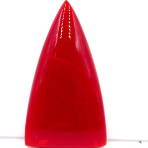 Puede incluir: Una piedra preciosa cabujón triangular de color rojo brillante con una superficie lisa y pulida.