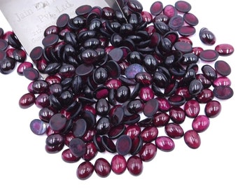May include: A pile of oval-shaped, dark red gemstones. The gemstones are smooth and shiny, with a slight variation in size and shape.