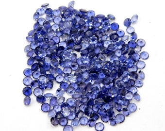May include: A large pile of loose round blue gemstones. The gemstones are faceted and have a light blue color.