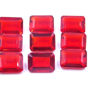 May include: Eight red, rectangular, faceted glass gems. The gems are arranged in three rows, with three gems in the top and bottom rows and two gems in the middle row.