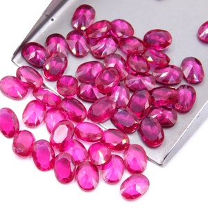 Op de afbeelding: Een grote groep ovale, gefacetteerde, roze edelstenen. De edelstenen zijn verspreid over een zilveren dienblad.