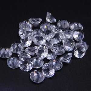 Puede incluir: Un montón de piedras preciosas redondas, transparentes y facetadas sobre un fondo negro. Las piedras preciosas son de varios tamaños y formas, y todas son muy brillantes.