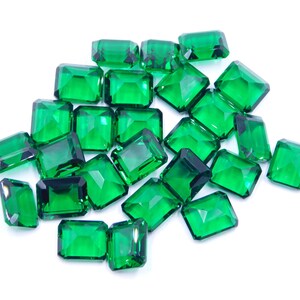 Könnte beinhalten: Ein Haufen smaragdgrüner, facettierter Glassteine, die Edelsteinen ähneln, auf weißem Hintergrund.