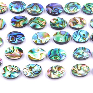 Könnte beinhalten: Eine Sammlung von 25 ovalen Abalone-Muschel-Cabochons. Die Cabochons sind irisierend in Blautönen, Grüntönen und Goldtönen.