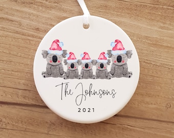 May include: White ceramic Christmas ornament with five gray koalas wearing red Santa hats. The ornament says "The Johnsons 2021".