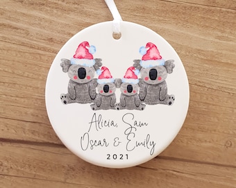 May include: White ceramic Christmas ornament with four gray koalas wearing red and white Santa hats. The ornament has the names "Alicia, Sam, Oscar & Emily" and the year "2021" written on it.