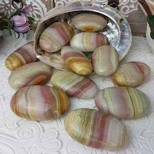Peut inclure: Ensemble de pierres polies de forme ovale, aux couleurs rose, crème, jaune et vert. Les pierres sont disposées dans et autour d'une coquille nacrée, suggérant un thème naturel ou décoratif.