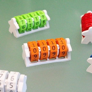 Könnte beinhalten: Sechs Punktezähler für Brettspiele, jeweils mit einer weißen, meeple-förmigen Kunststoffbasis und einem drehbaren Zahlenrad. Die Zähler sind in Violett, Grün, Orange, Rot, Blau und Weiß gehalten und mit schwarzen Ziffern auf den Rädern bedruckt.
