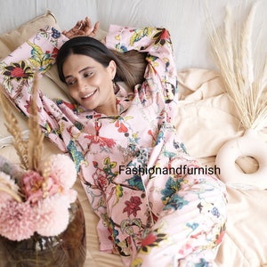 May include: A light pink pajama set featuring a vibrant floral pattern with red, yellow, blue, and green botanical motifs. The long-sleeved button-down top and matching trousers include the text Fashionandfurnish printed on the fabric.