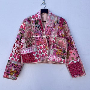 May include: A pink quilted jacket with a floral print and a contrasting white trim. The jacket has a V-neck and long sleeves.