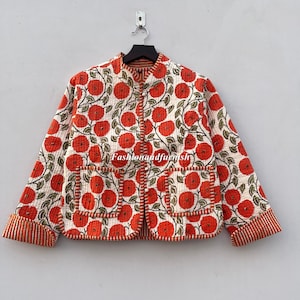 May include: A white quilted jacket with a floral print featuring orange flowers. The jacket has a mandarin collar, long sleeves, and two patch pockets. The seams are outlined in orange thread.