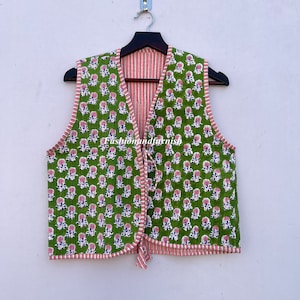 May include: A green quilted vest with a pink floral print and a red and white striped lining. The vest has a tie closure at the front.