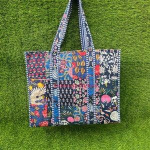 May include: A blue and white patchwork tote bag with floral and geometric patterns. The bag has a long handle and is made of quilted fabric.