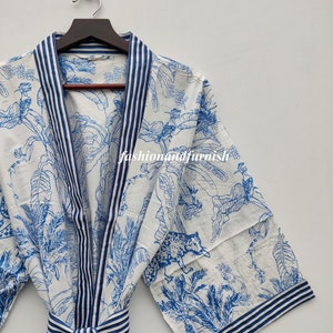 Op de afbeelding: Een witte katoenen badjas met een blauw-witte gestreepte rand en een blauw-witte jungleprint met bladeren, vogels en een luipaard. De badjas heeft een strikceintuur.