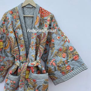 Puede incluir: Bata acolchada azul claro con un estampado floral en tonos naranja, amarillo y rosa. La bata tiene un ribete a rayas y un cinturón a juego. El texto "fashionandfurnish" es visible.