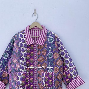 May include: A purple and white quilted jacket with a floral print. The jacket has a button-up front and a collar. The sleeves have a striped pattern.