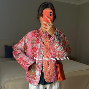 May include: A pink quilted jacket with floral embroidery and orange trim. The jacket is worn with white trousers and a small orange crossbody bag. The text "Fashionandfurnish" is visible in the image.