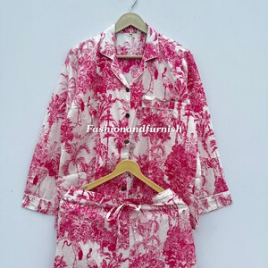 May include: A two-piece pajama set in white and pink. The set includes a long-sleeved button-down shirt and drawstring shorts. The fabric features a pink toile pattern with trees, birds, and other natural elements. The text "Fashionandfurnish" is visible.