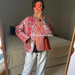 Può includere: Giacca trapuntata rosa con ricami floreali e finiture arancioni. La giacca è abbinata a pantaloni bianchi e una piccola borsa a tracolla arancione. Il testo "Fashionandfurnish" è visibile.