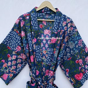 May include: A blue floral patterned robe with pink and green accents. The robe is made of a soft fabric and has a tie closure. The robe is hanging on a wooden hanger.