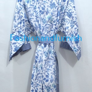May include: A white cotton robe with a blue floral print and blue and white striped trim. The robe has a sash tie at the waist.