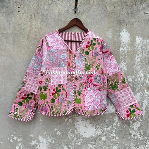 May include: A quilted jacket featuring a patchwork design with various pink, white, and green floral and geometric patterns. The jacket has a V-neckline, long sleeves, and a front button closure with a striped trim. The text Fashionandfurnish is visible.