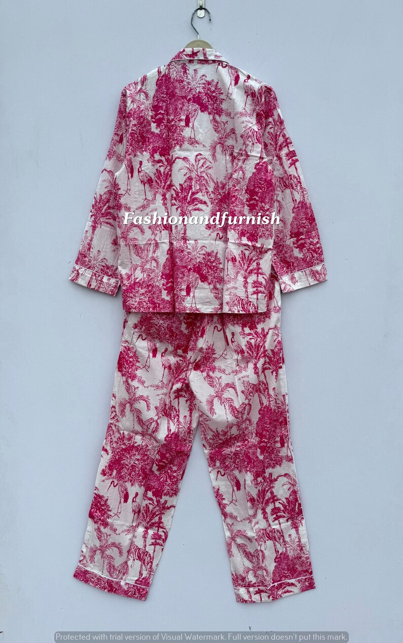 May include: A two-piece pajama set in white and fuchsia. The set includes a long-sleeved button-down shirt and matching pants. The fabric features a repeating pattern of tropical trees, birds, and other foliage. The text "Fashionandfurnish" is visible on the shirt.