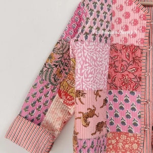 May include: A pink and white quilted jacket with a patchwork design featuring floral and tiger prints. The jacket has a mandarin collar and a button closure.