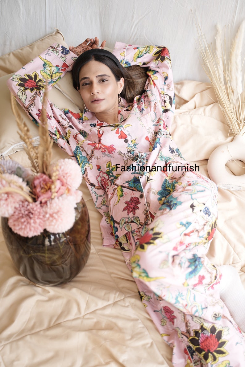 May include: A light pink long-sleeve pajama set featuring a vibrant floral and botanical print in shades of red, yellow, blue, and green. The button-down shirt has a collar and white piping. The text Fashionandfurnish is visible.