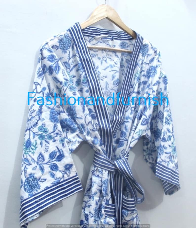 May include: A white cotton robe with a blue floral print and blue and white striped trim. The robe has a tie belt and long sleeves.