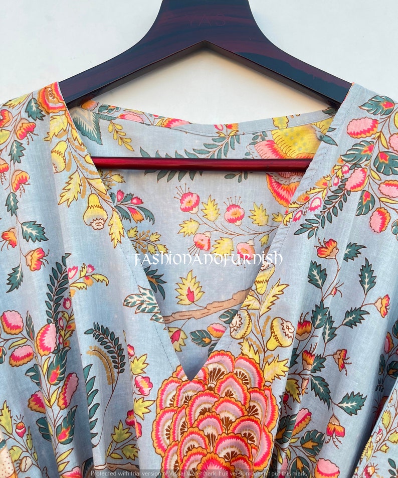 Puede incluir: Prenda azul claro con estampado floral, con flores y hojas rosas, amarillas y verdes. Se aprecia el cuello en V. La prenda est&aacute; colgada en una percha de madera oscura.