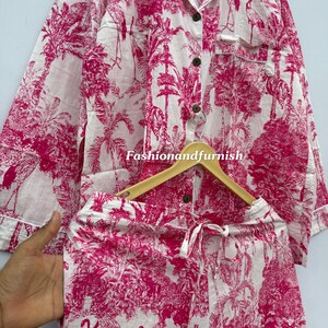 May include: A two-piece pajama set in white and fuchsia. The set features a button-down shirt with a chest pocket and shorts with a drawstring waist. The fabric is printed with a tropical scene of trees and birds. The text "Fashionandfurnish" is visible.