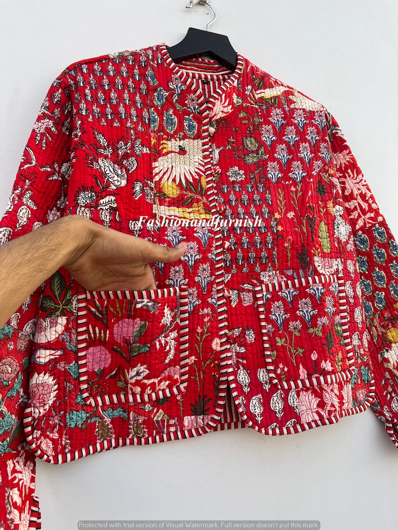 May include: A red quilted jacket with a floral print and a mandarin collar. The jacket has a button closure and a pocket on the left side.