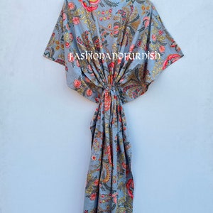 Puede incluir: Un vestido caft&aacute;n gris con estampado floral, colgado de una percha negra. El patr&oacute;n floral incluye flores rojas, amarillas y verdes. El texto "FASHIONADOFURDISH" es visible. El vestido es de tejido ligero.