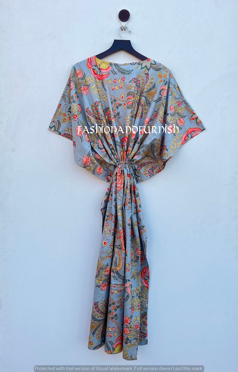 Puede incluir: Un vestido caft&aacute;n gris con estampado floral, colgado de una percha negra. El patr&oacute;n floral incluye flores rojas, amarillas y verdes. El texto "FASHIONADOFURDISH" es visible. El vestido es de tejido ligero.
