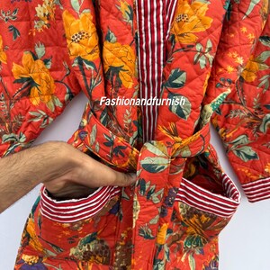 May include: A quilted, red floral robe with yellow and blue flowers. The robe has a striped interior and trim, with a matching belt and pockets. The robe is made of a soft, quilted fabric.