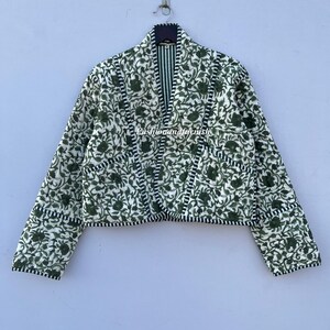 以下が含まれることがあります： 白と緑のフローラルプリントのキルティングジャケット。黒と白のストライプの裏地が付いています。ジャケットはVネックで長袖です。