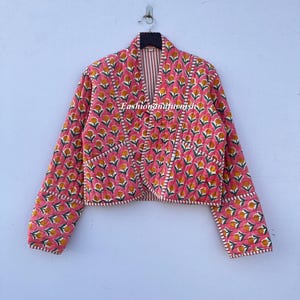 May include: A pink quilted jacket with a floral print and white trim. The jacket has a V-neck and long sleeves.