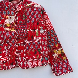 May include: A red quilted jacket with a floral print and white trim. The jacket has a mandarin collar and a button closure. The fabric is a patchwork of different floral patterns.