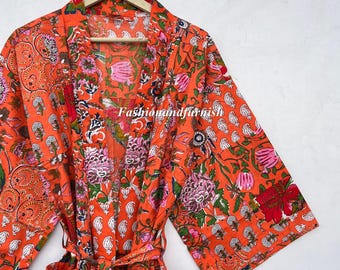 Op de afbeelding: Oranje badjas met bloemenprint en bijpassende riem, hangend aan een houten hanger. Het patroon heeft roze, groene en witte bloemen en paisley-ontwerpen. De tekst "fashionandfurnish" is zichtbaar op de badjas.