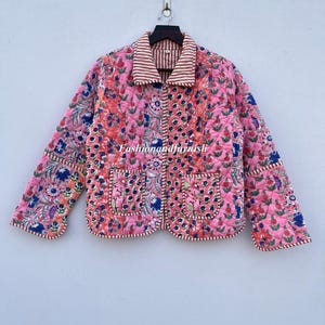 Op de afbeelding: Een roze gewatteerd jack met een bloemenprint en een gestreepte kraag. Het jack heeft twee zakken aan de voorkant en een ritssluiting.