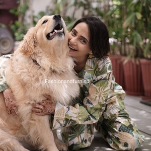 May include: A woman wearing a green and white patterned pyjama set is smiling and hugging a golden retriever dog. The dog is looking up at the woman.