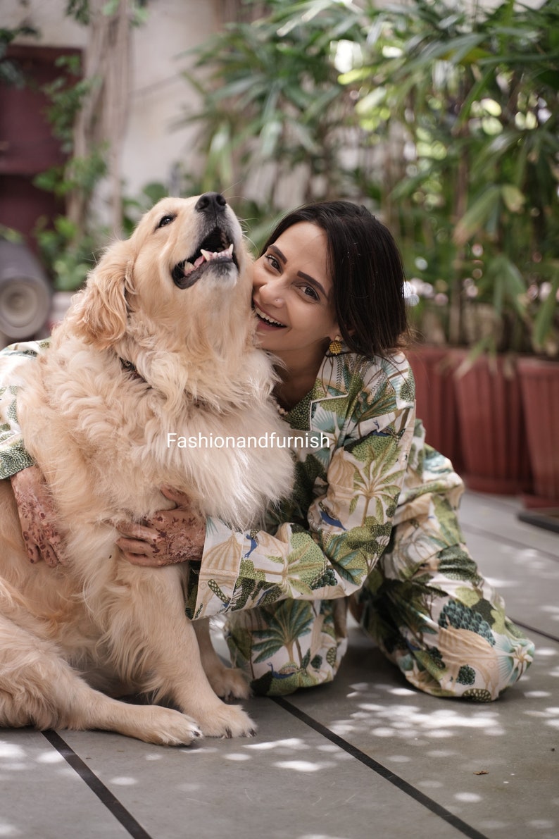 May include: A woman wearing a green and white patterned pyjama set is smiling and hugging a golden retriever dog. The dog is looking up at the woman.