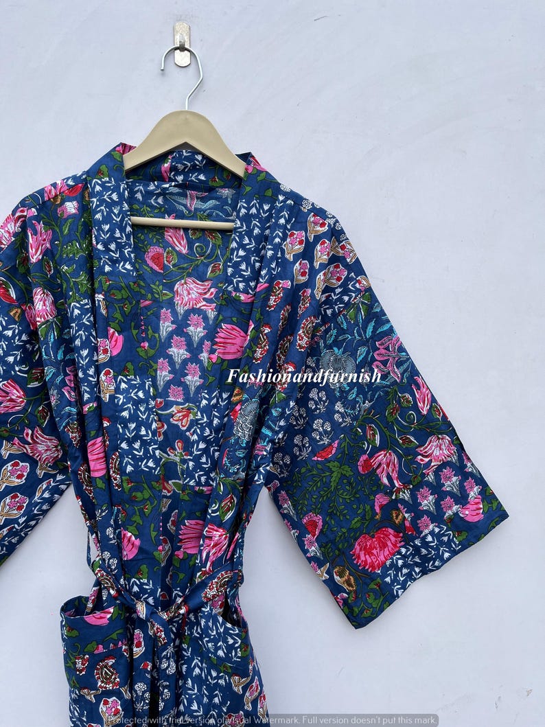 May include: A blue floral print robe with a matching belt, hanging on a wooden hanger. The robe features a vibrant pattern of pink flowers and green leaves against a dark blue background. The text "Fashionandfurnish" is visible.