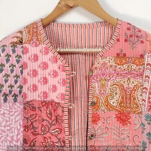 May include: A pink quilted jacket with a striped front and a patchwork design featuring various floral patterns. The jacket has a button closure and a V-neck.