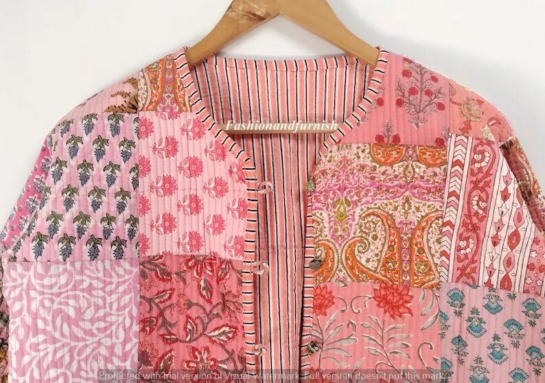 May include: A pink quilted jacket with a striped front and a patchwork design featuring various floral patterns. The jacket has a button closure and a V-neck.