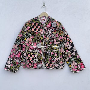 Puede incluir: Chaqueta acolchada negra con un estampado floral en rosa, verde y blanco. La chaqueta tiene cuello redondo, mangas largas y dos bolsillos delanteros. Los bordes están adornados con un patrón de rayas blancas y negras. El texto "fashionandfurnish" es visible.