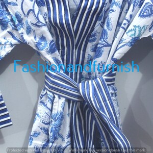 May include: A white cotton robe with blue floral print and blue and white striped trim. The robe has a tie belt and long sleeves.