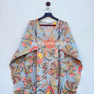 Puede incluir: Un vestido caft&aacute;n gris con estampado floral, con cuello en V y mangas anchas. La tela presenta un patr&oacute;n de flores y follaje rosas, amarillas y naranjas. El texto "FASHIONADOKIRISH" est&aacute; impreso en la prenda.