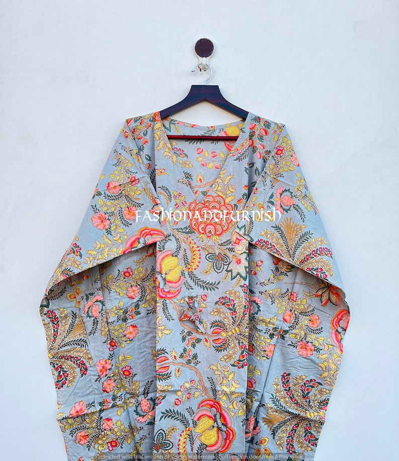 Puede incluir: Un vestido caft&aacute;n gris con estampado floral, con cuello en V y mangas anchas. La tela presenta un patr&oacute;n de flores y follaje rosas, amarillas y naranjas. El texto "FASHIONADOKIRISH" est&aacute; impreso en la prenda.